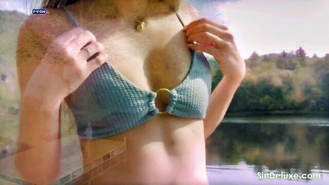 Brunette teases by pulling down teal bikini top exposing cleavage outdoors by lake