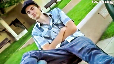 Relaxed young guy in plaid shirt and jeans lounging on park bench with sneakers out for foot worship