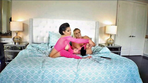 Lesbian babes in sheer pink lingerie toy inserting black dildo into wet shaved pussy on bed