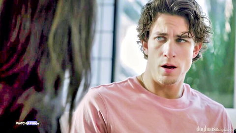Curly-haired guy in pink shirt looks shocked at long-haired brunette woman close-up indoors
