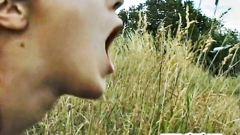 Closeup of blonde woman screaming with mouth wide open and tongue out in outdoor grass field