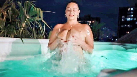 Topless brunette PAWG with big tits splashes in glowing outdoor hot tub