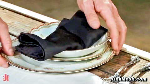 Hands folding black napkin into white porcelain bowl on floral plate during table setting