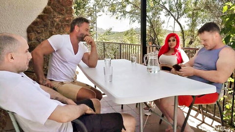 Busty redhead MILF with huge fake tits in skimpy top surrounded by three older men at outdoor table