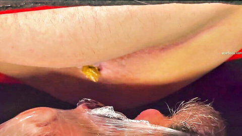 Hairy woman's stretched asshole with yellow anal plug protruding over man's cum-dripping open mouth