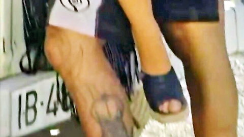 Sexy woman's fringed espadrille feet and legs teasing tattooed man's hairy calves outdoors