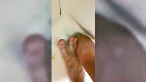 Blurry close-up of feet and pink genitals being washed in bubbly bath