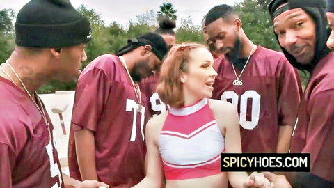 Redhead cheerleader in uniform surrounded by black men in jerseys for group sex