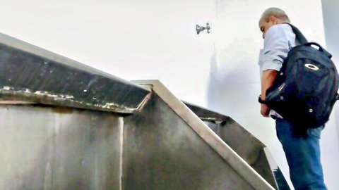 Mature man in white shirt and jeans stands in public toilet with backpack