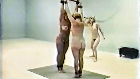 Three naked blonde women bound with arms raised in restraints