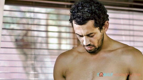 Muscular shirtless hunk with curly hair and ripped abs gazing down intensely