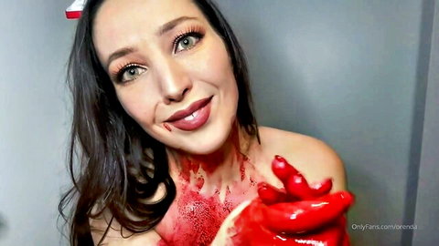 Topless woman with fake blood dripping on tits and face smiling while holding bloody red glove