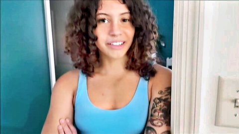 Smiling curly-haired tattooed babe teasing her perky tits in tight blue tank top