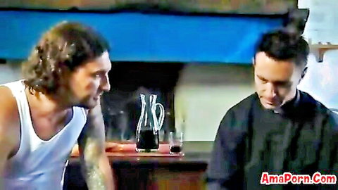 Tattooed muscular hunk in tank top leans toward priest over wine at kitchen table