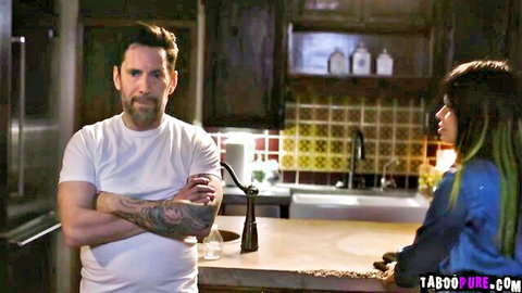 Tom confronts Tanya in kitchen, tattooed man in white tee faces long-haired woman in blue top