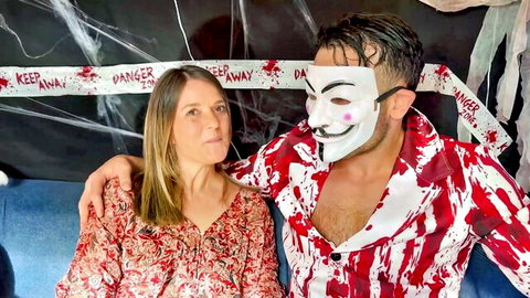 Brunette woman in red floral dress poses intimately with masked man in bloody shirt on Halloween