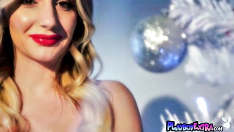 Seductive blonde babe with red lips smiling playfully amid Christmas ornaments