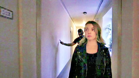 Blonde woman in leather jacket stalked by masked man sneaking up in hotel hallway