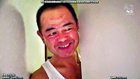 Mischievous Asian man peeking through door crack with sly smile in white tank top