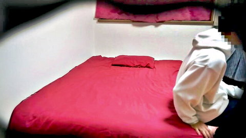 Asian couple in hoodies sitting on red bed in cozy room teasing foreplay