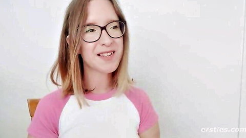 Cute glasses-wearing redhead teen smiling playfully in pink baseball shirt