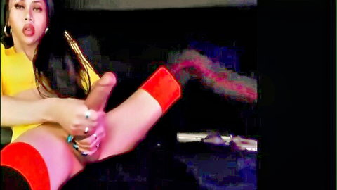 Asian transgender woman in yellow top and red stockings stroking huge cock