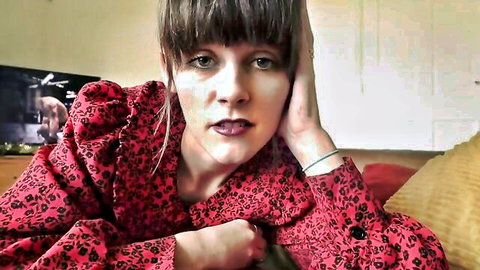 Brunette MILF with bangs pouting seductively in red floral blouse on couch
