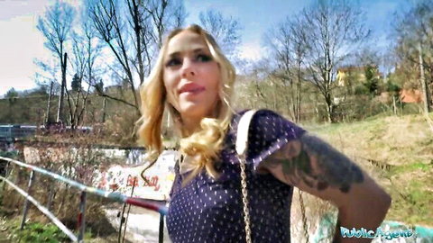 Smiling blonde babe with tattoos in polka-dot dress outdoors near graffiti bridge