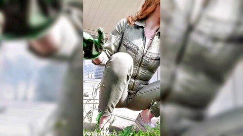 Mandy Frizzle in gray jumpsuit, squatting outdoors with gloves, teasing pose