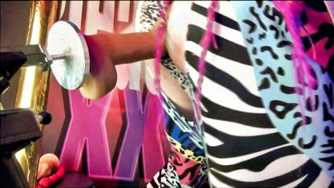 Curvy black woman with colorful hair bent over, hand pressing suction dildo to her exposed ass