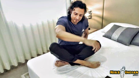 Curly-haired Indian man in t-shirt on bed, Airbnb guest with big ass host