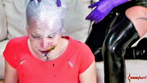 Latex-gloved dominatrix grabs plastic-wrapped head of messy-faced submissive in BDSM punishment