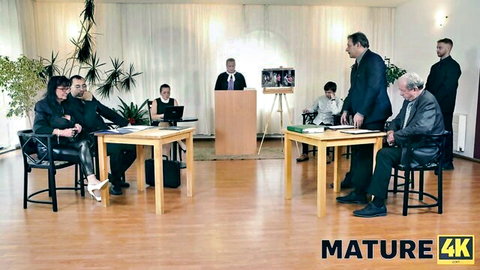 Mature women in leather skirts and suits negotiate at tables with older men in formal room