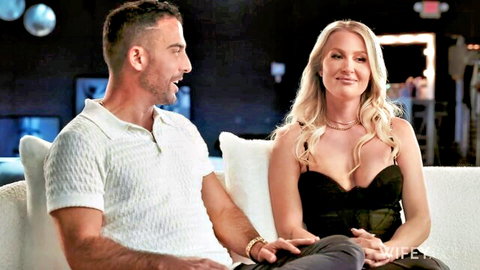 Curvy blonde MILF with huge tits smiles intimately as man touches her thigh on couch