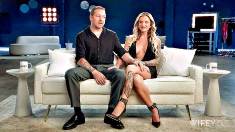 Blonde wife in low-cut black dress with tattooed husband on couch