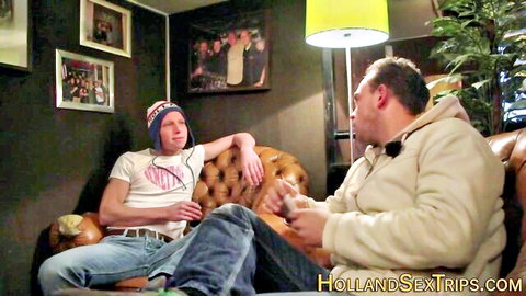 Two casually dressed men chatting on leather couch in dimly lit room