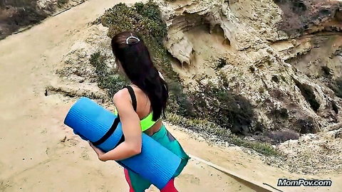 Fit brunette in activewear hikes coastal trail with yoga mat, ready for beach session