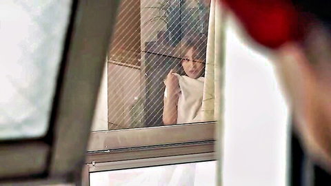 Voyeur view of sensual Japanese woman smiling teasingly through window in tight white sweater