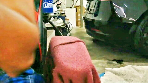 Damaged black car in garage with Loctite container and red towel draped nearby