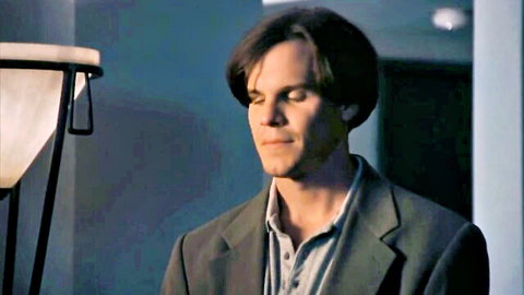 Handsome man in open-collar suit gazing thoughtfully in dimly lit room
