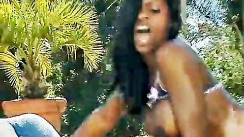 Ebony woman with long black hair in purple bikini, seductive outdoor pose by pool