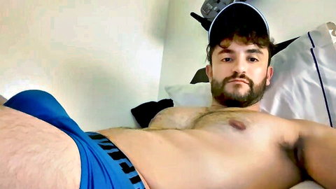 Muscular bearded gay hunk bulging in tight blue underwear on bed