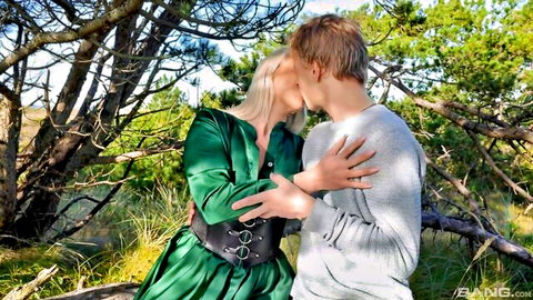 Blonde babe in sexy green dress passionately kissing hunk outdoors in forest