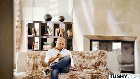 Bald Asian man in open white shirt sitting casually on furry couch in luxury living room