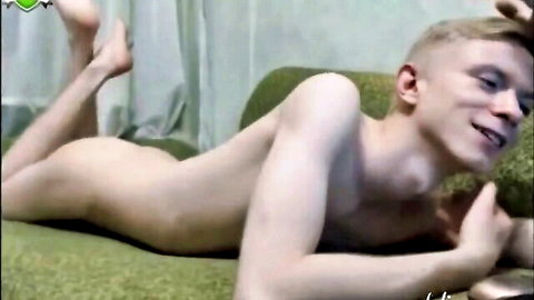 Smiling nude blonde twink lying sideways on green couch exposing bare ass and slim body