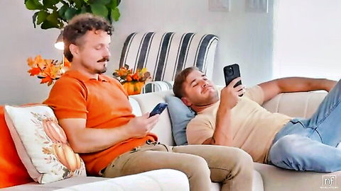 Two handsome white men lounging on couch, checking phones on Thanksgiving