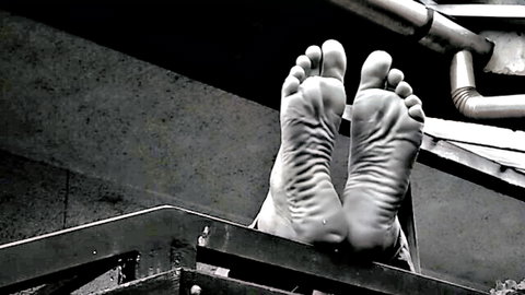 Close-up of sexy bare male feet soles and toes soles-up in black and white outdoor shot