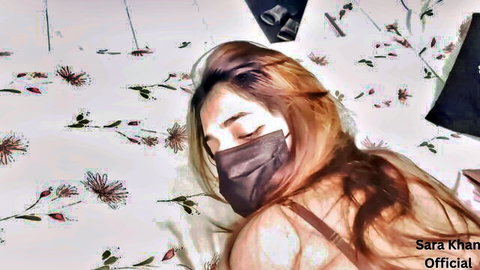 Sexy Indian MILF Sara Khan lying seductively on bed with mask exposing cleavage