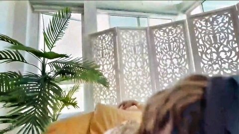 Blonde woman with wild hair lying face down on yellow fabric in room with plants