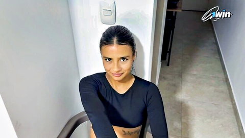 Sexy brunette in tight black crop top smiling teasingly with tattooed midriff visible
